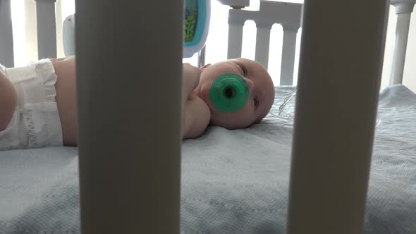 A swaddled baby sucking on a pacifier in a hospital crib.  He starts to cry when he drops his pacifi