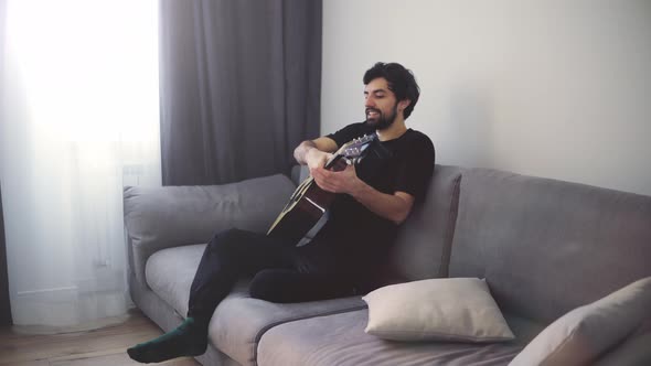 A Young Man Sits on the Couch and Plays the Guitar