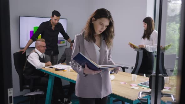 Concentrated Beautiful Caucasian Woman Analyzing Documents Standing in Office with Multiethnic