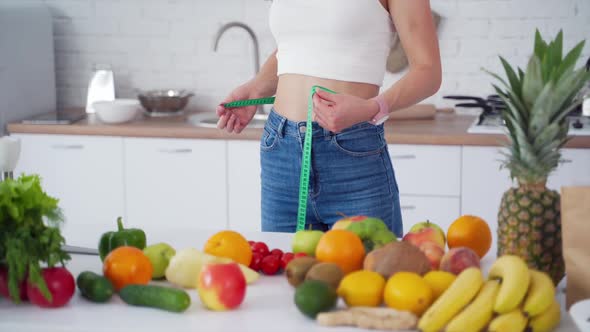 Dieting concept. Young woman measures her belly in the kitchen. 