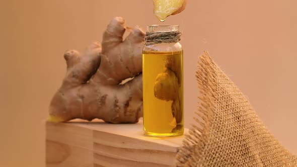 Glass Bottle of Essential Ginger Oil Dripping Ginger Root on Beige Background
