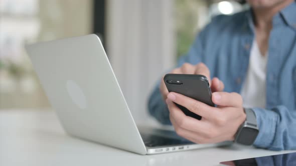 Close Up of Male Hand with Laptop Using Smartphone