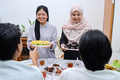 Excited asian woman muslim serving food for break fasting dinner during iftar ramadan - PhotoDune Item for Sale