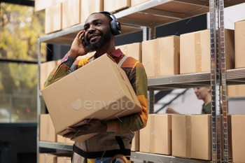 ening music at headphones, preparing customers orders during work shift in storage room. African american manager working at products shipment