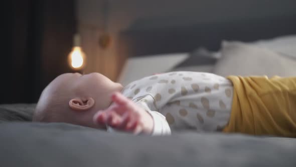 Unhappy crying baby lying on big bed with soft blanket indoors, low angle side shot