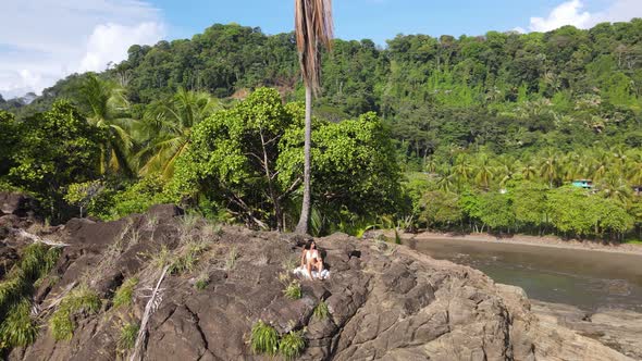 Wide aerial view of a lady sitting and resting on a cliff edge, Costa Rica