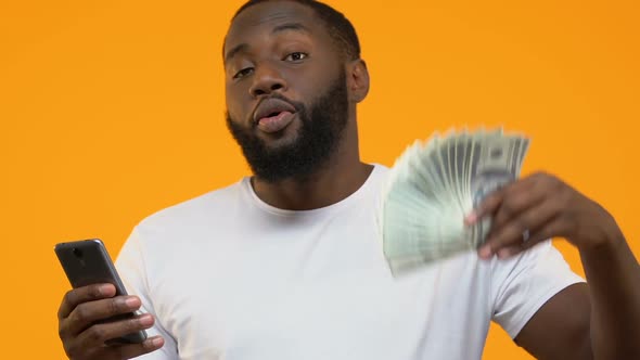 Black Male Using Smartphone Application Showing Dollar Bills, Cash Back Service