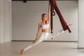 A girl in white sportswear does yoga on a hanging hammock in the fitness room - PhotoDune Item for Sale