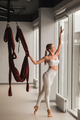 Portrait of a girl in white sportswear Standing near the window and holding a hanging hammock in her - PhotoDune Item for Sale