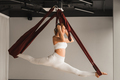 A girl in white sportswear does yoga on a hanging hammock in the fitness room - PhotoDune Item for Sale