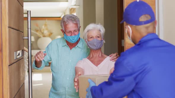 Delivery man delivering package to senior caucasian couple wearing face masks at home