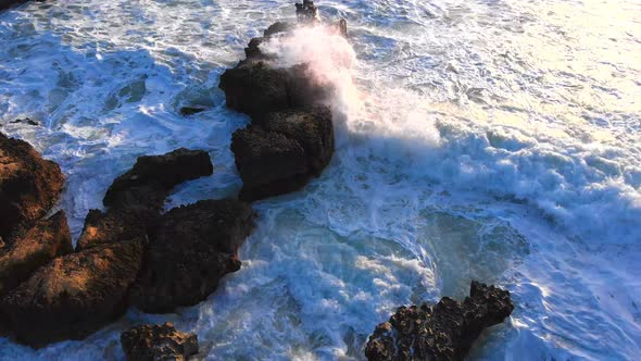 Aerial drone view of rough waves crashing the rocky shoreline