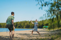 caucasian man and teenager son playing badminton on the lakeside. Parents and teens concept.  - PhotoDune Item for Sale