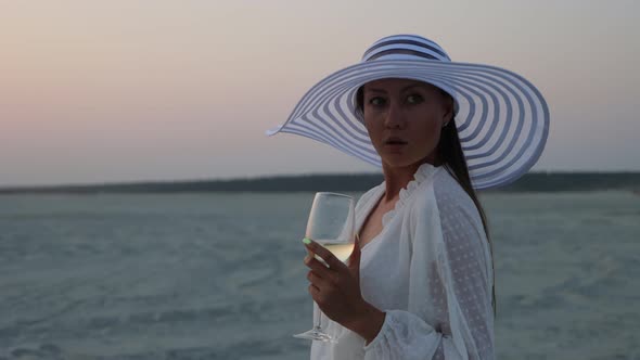 Elegant Woman with Glass of Wine Resting on Beach at Sunset