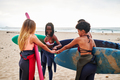 Four surfer friends holding their surfboards as they fist bump together on the beach - PhotoDune Item for Sale