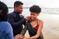 A young man helping to dress his female surfer friend in her wetsuit on the beach - PhotoDune Item for Sale