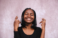 Portrait of afro woman on a brown background with eyes closed and fingers crossed.port - PhotoDune Item for Sale