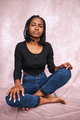 Afro woman sitting on studio floor on brown background looking at camera. - PhotoDune Item for Sale