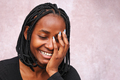 Portrait on a brown background of Afro woman laughing, eyes closed and one hand on her face. - PhotoDune Item for Sale