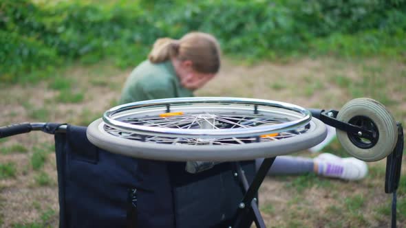 Wheel of Rolled Over Wheelchair Spinning with Blurred Disabled Girl Crying at Background