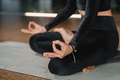 Close-up of the legs and arms of a woman in a black tracksuit sitting on a yoga mat  - PhotoDune Item for Sale