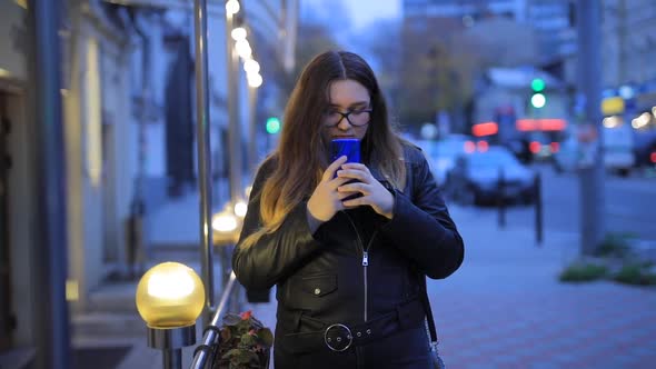 Woman Is Chatting in the Smartphone Against the Background of the Evening City