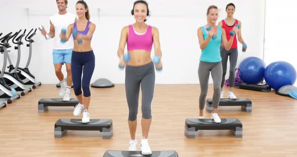 Aerobics Class Stepping Together Led by Instructor and Lifting Dumbbells