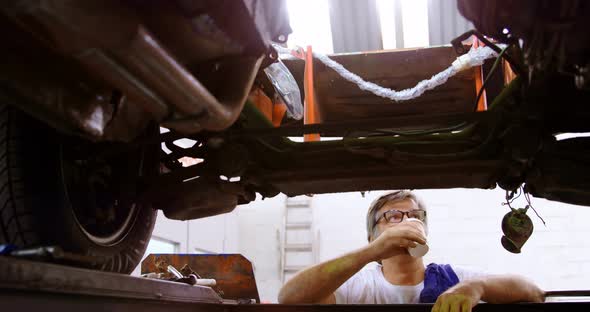 Male mechanic having coffee while servicing a car 4k