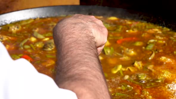 A traditional Spanish dish is being stirred by the cook holding the ladle, POV slow motion shot, in