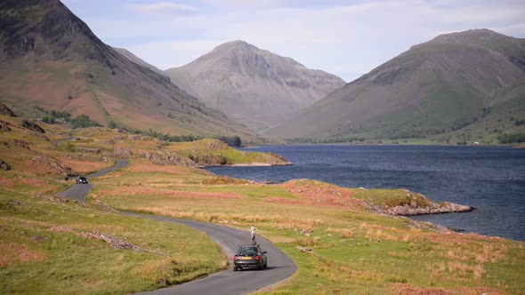 People driving on a road by the lake towards the mountains of the England Lake District - wide shot