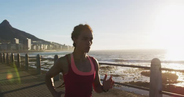 African american woman running on promenade by the sea at sundown