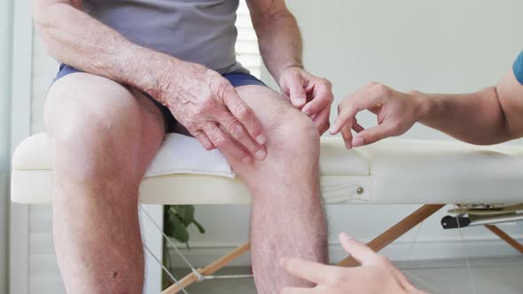 Male physiotherapist examining knee joint of senior man on examination table at studio