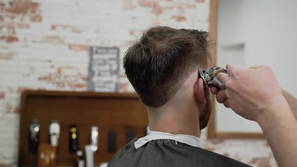 Man Barber Cutting Hair of Male Client with Clipper at Barber Shop