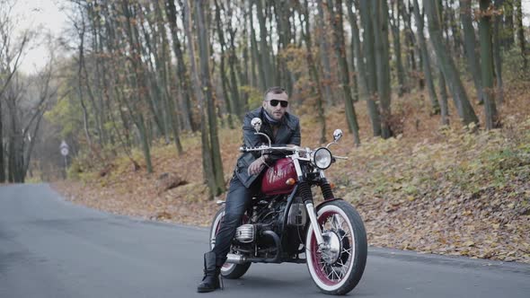 Portrait of Brutal Biker in Sunglasses and Leather on Motorcycle on Roadway