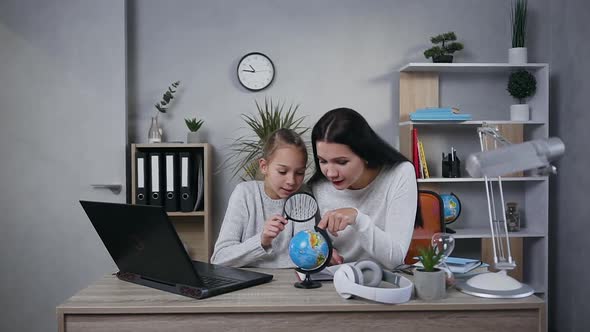 Smiling Mother and Teenage Daughter Looking on Small Globe through the Magnifier at Home