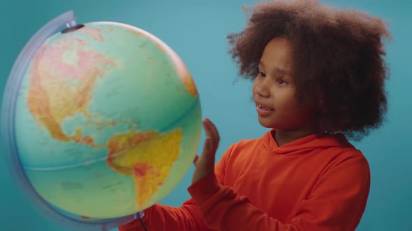 Curious African American school girl exploring the globe standing on blue background