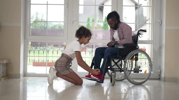 Wide Shot Positive Teenage African American Daughter Taking Care of Disabled Father Tying Shoelaces