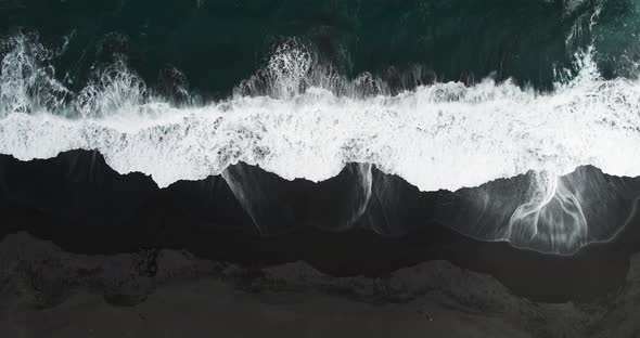 Overhead view of waves on a black sand beach with people walking on the shore