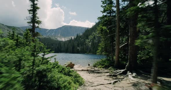 Aerial of lake in basin of pine covered mountains and in the distance snow covered peaks.