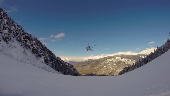 A helicopter lands to pick up skiers in the mountains.