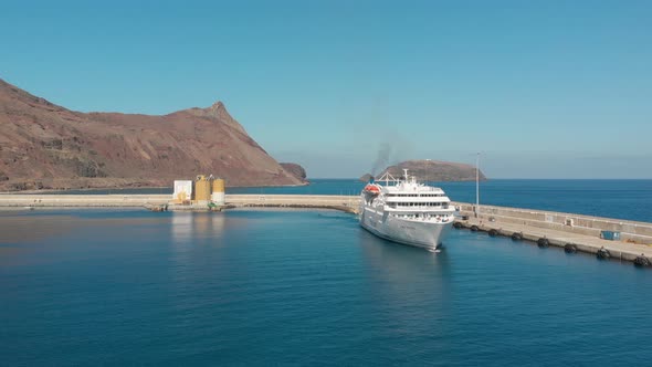 Aerial shot over Passenger boat leaving marina with island cliffs as background