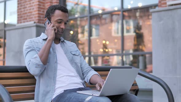 African Man Talking on Phone Sitting on Bench