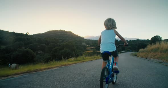 Carefree Child Boy Cycling on Bike at Empty Country Road on Summer Vacations