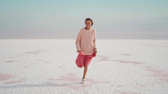 Happy Smiling Woman in Pink Oversize Wear Running on Camera on White Salty Desert Background of