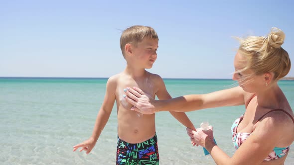 Cute Mother Puts Sunscreen Lotion on the Baby Azure Sea and Blue Sky in the Background Protection