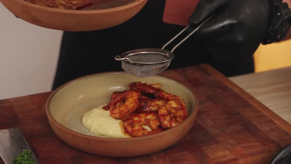 Faceless chef using a food strainer straining the sauce, adding the liquid into a plated seafood gou