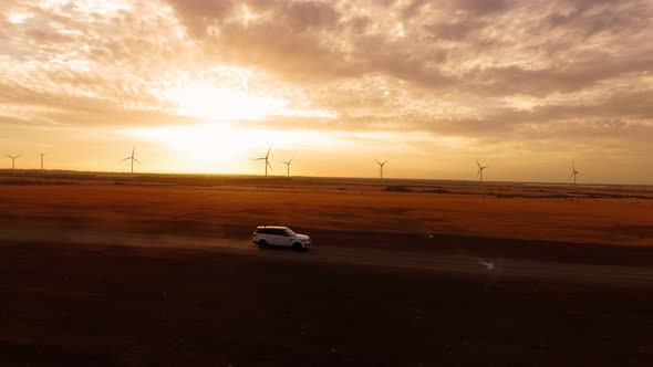 Aerial View Car Drives in Field Against Backdrop Windmill and Beautiful Sunset