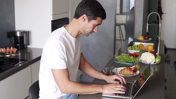 Brunette Young Man Sit and Use Laptop Work in the Morning at Home in Kitchen Counter