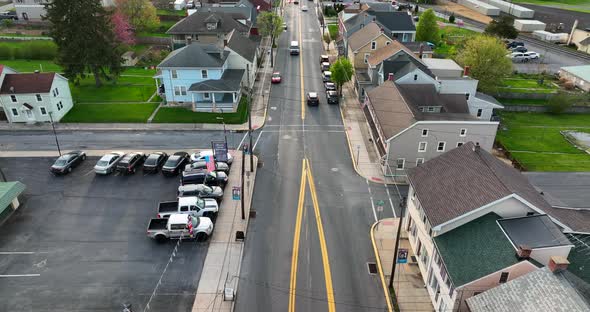 Car dealership in small town USA. American flag and old homes by street. Aerial reverse dolly at spr