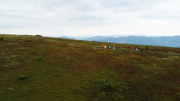 Tourists in Raincoats Go on a Mountain Range